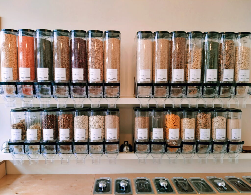 Zero waste shopping - A wall full of dispensers containing a variety of nuts, seeds, pasta, rice, beans and other foods for refilling containers.