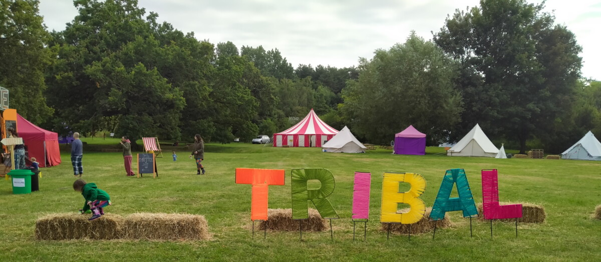 Photo of field with large, colourful letters reading 'Tribal' and young child playing on a bail of straw.